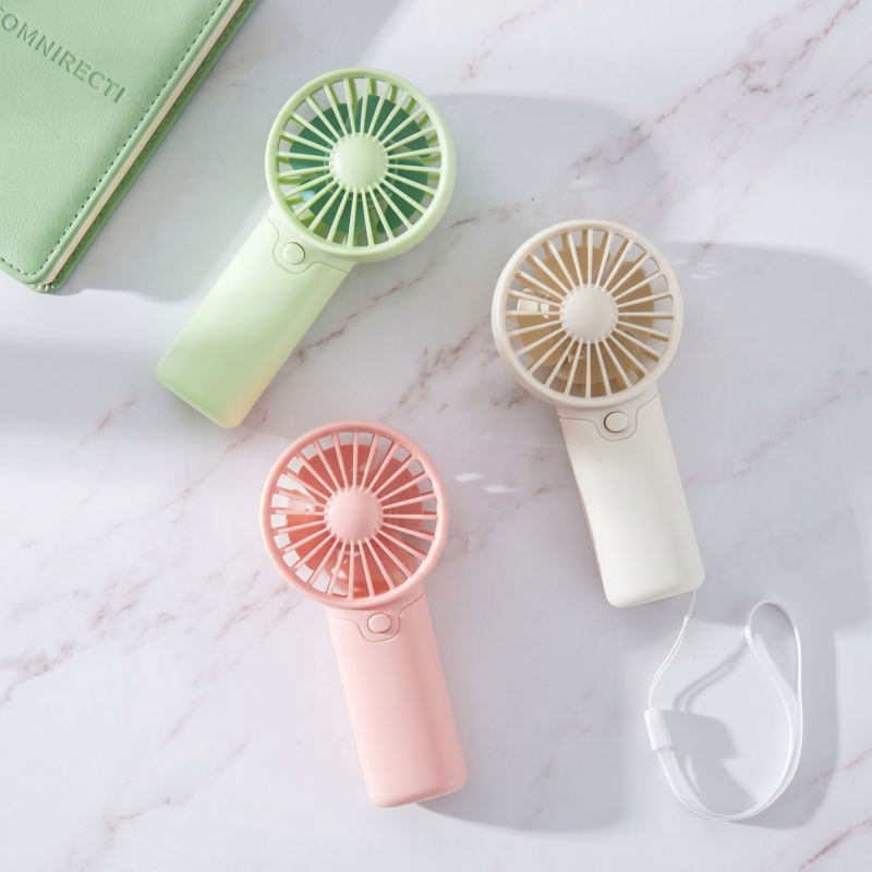 Three Retailark creative handheld fans in pink, green, and white laid out on a marble surface